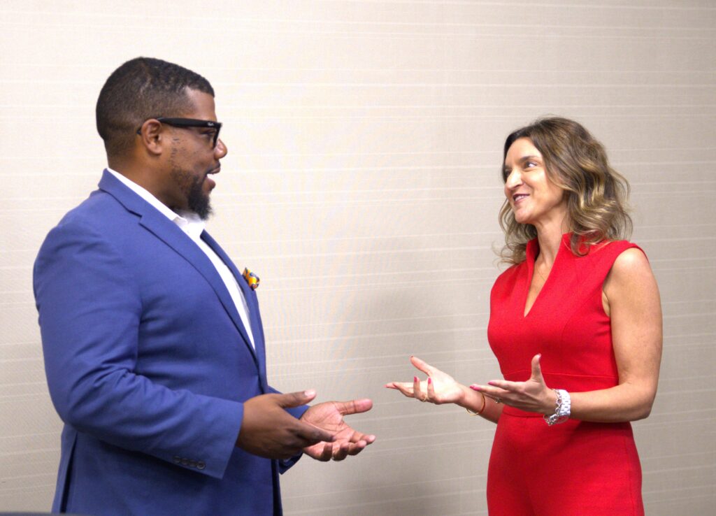 Man in blue suit and woman in red dress speaking with open gestures